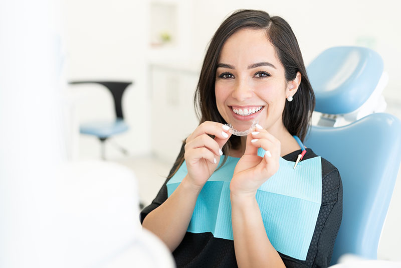 a smiling, brunette woman in her 30's holding Invisalign